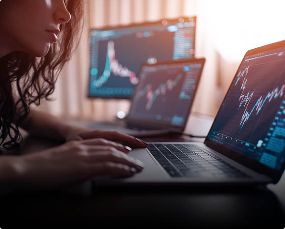 young female trader with laptop and screen looking at stock charts