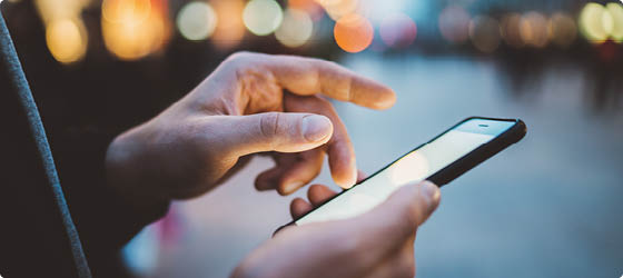 Close-up image of male hands using smartphone at night on city shopping street, searching or social networks concept, hipster man typing an sms message to his friends