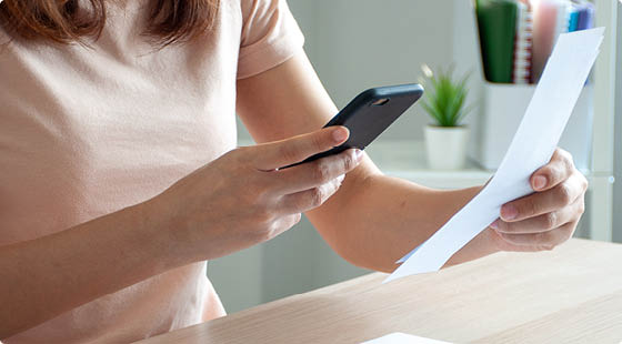 A woman uses a smartphone to scan the barcode to pay monthly phone bills after receiving an invoice sent to home  Online bill payment concept