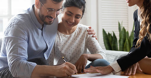 Horizontal view happy married couple Caucasian husband Indian ethnicity wife signing rental contract at meeting with realtor or landlord, first property purchase, mortgage and loan ownership concept