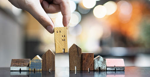 Hand choosing mini wood house model from model and row of coin money on wood table, selective focus, Planning to buy property  Choose what's the best  A symbol for construction ,ecology, loan concepts