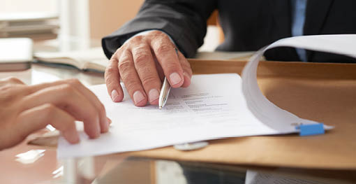 Close-up of businessman examining business contract and signing it at the office desk