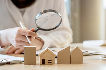 Looking for real estate agency, property insurance, mortgage loan or new house  Woman with magnifying glass over a wooden house at her office
